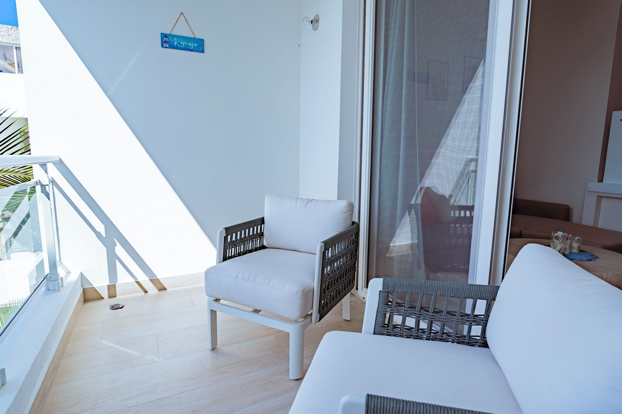 Un balcón con una silla blanca, una silla de mimbre y un letrero que dice 'Renzo'.