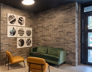 Ein Zimmer mit Backsteinwand, einem grünen Sofa, zwei gelben Sesseln und gerahmten Bildern.