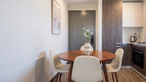 A modern kitchen with wooden cabinets, a stove, and a dining area with a wooden table and white chairs. - Parque Los Reyes - Domus Travels (Santiago)