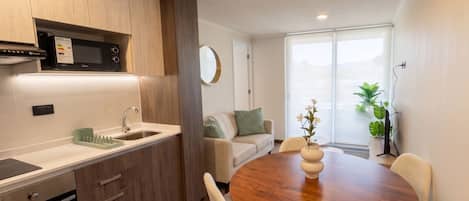 Una cocina moderna con microondas integrado, un lavamanos y una zona de comedor con mesa y sillas de madera.