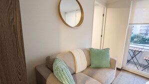 A living room with a beige sofa, a round mirror, and a view of a balcony. - Parque Los Reyes - Domus Travels (Santiago)