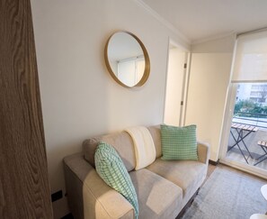 Ein Wohnzimmer mit einem beigen Sofa, einem runden Spiegel und Blick auf einen Balkon.