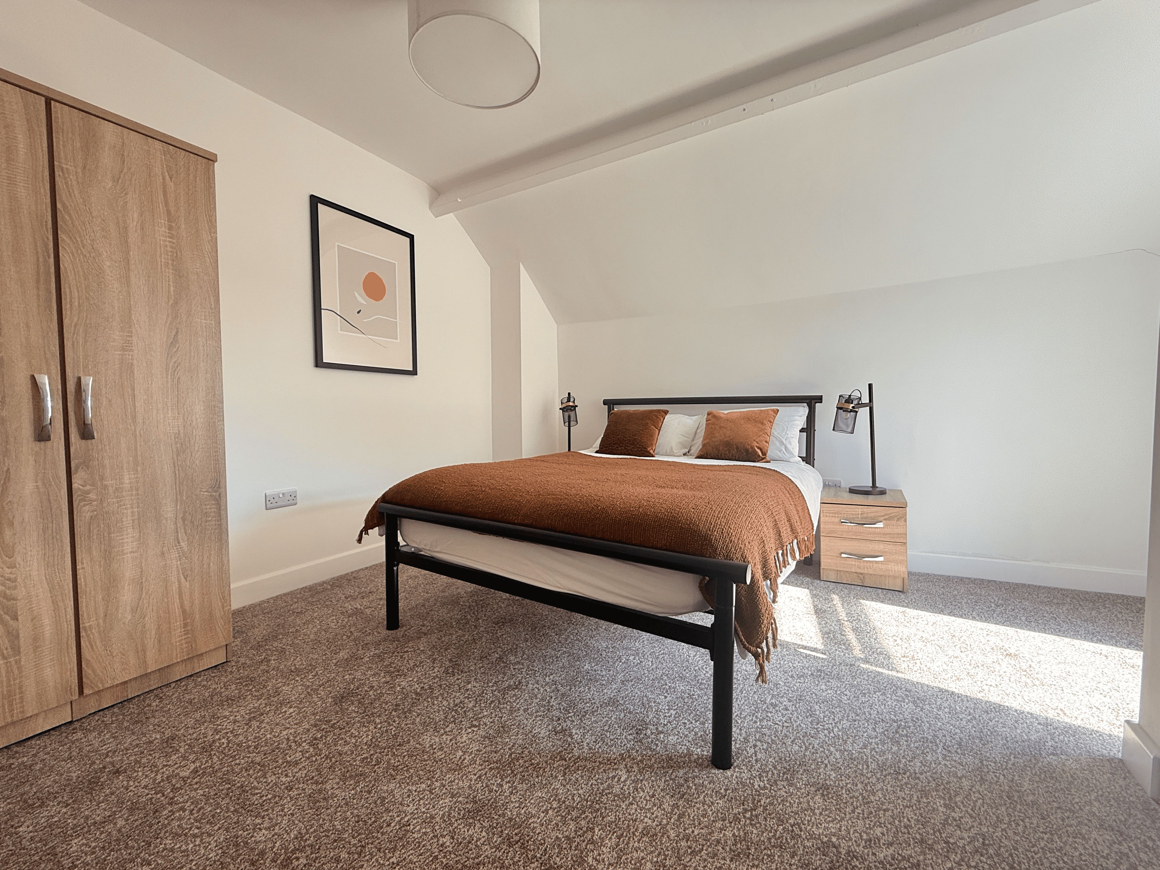 A bedroom with a bed, a wardrobe, a bedside table, and a lamp.
