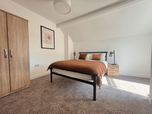 Een slaapkamer met een bed, een kledingkast, een nachtkastje en een lamp.
