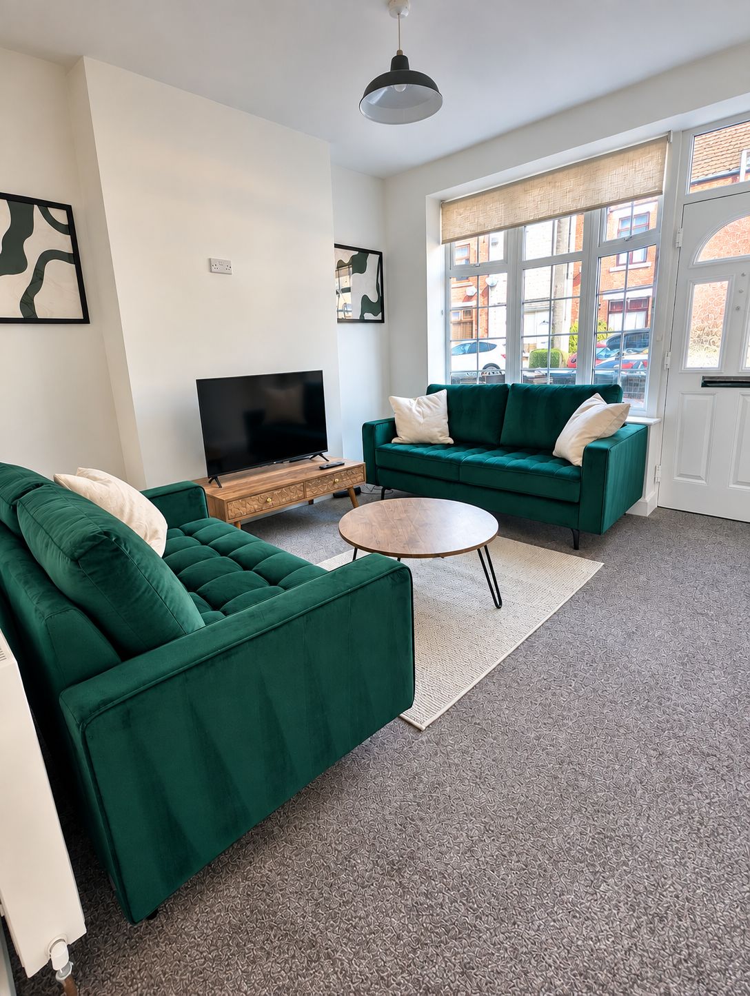 A living room with a green sofa set, a flat-screen TV on a wooden stand, and a round coffee table.