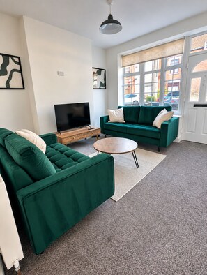 A living room with a green sofa set, a flat-screen TV on a wooden stand, and a round coffee table.