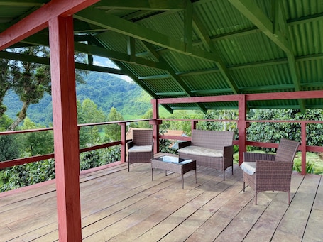 A covered outdoor seating area with wicker furniture and a view of a lush green landscape.