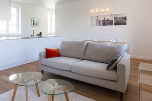 A modern living room with a sofa, glass coffee tables, and a dining area with a table set for two. - Renovated two-bedroom apartment just a stone's throw from the Marché Central (La Rochelle)