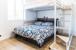 Ein Stockbett mit gemustertem Bettbezug, einem Kopfteil und einem weißen Regalelement.