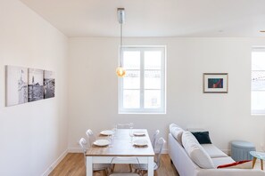 Ein Essbereich mit einem Holztisch, gedeckt für vier Personen, einer Couch und einem Fenster mit Tageslicht.