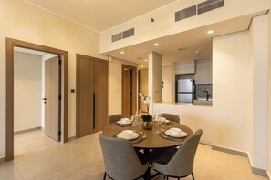 Un coin repas avec une table ronde dressée pour quatre personnes, une cuisine en arrière-plan et une porte donnant sur une autre pièce.