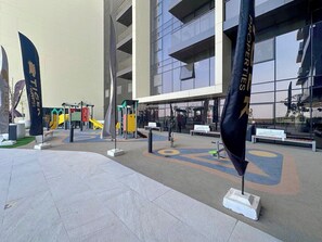 An outdoor area with a playground, seating, and flags. - Brand-New 1BR in Neva Residence | Near Circle Mall (Dubai)