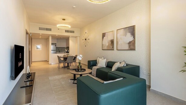 A modern living room with a sofa set, a flat-screen TV, and a dining area. - Brand-New 1BR in Neva Residence | Near Circle Mall (Dubai)