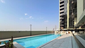 A rooftop swimming pool with a clear sky, surrounded by a modern building with balconies. - Brand-New 1BR in Neva Residence | Near Circle Mall (Dubai)