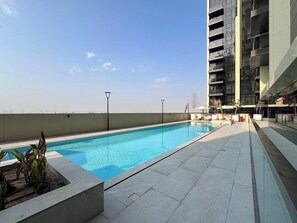 Ein Pool auf dem Dach mit blauem Himmel, umgeben von einem modernen Gebäude mit Balkonen.