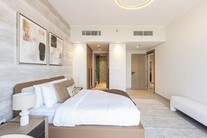 A modern hotel room with a large bed, a bedside table, a lamp, and a wall-mounted artwork. - Brand-New 1BR in Neva Residence | Near Circle Mall (Dubai)