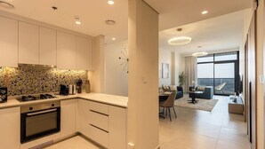 A modern kitchen with white cabinets, a built-in oven, and a backsplash with a mosaic pattern. - Brand-New 1BR in Neva Residence | Near Circle Mall (Dubai)