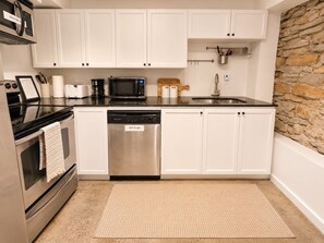 A kitchen with white cabinets, a stainless steel dishwasher, a microwave, and a stone wall backsplash. - Modern Loft-Style Basement Bright & Spacious (Toronto)