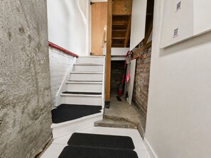 A narrow stairway with a wooden beam ceiling, white walls, and a brick wall on one side. - Modern Loft-Style Basement Bright & Spacious (Toronto)