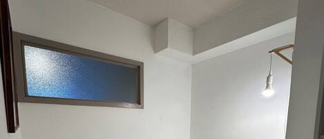 Une petite chambre avec un lit simple, une fenêtre, un luminaire suspendu et un plancher en bois.