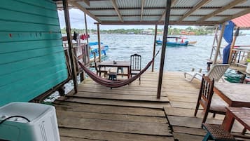 Un muelle de madera con una hamaca, una mesa y sillas, con vista a un cuerpo de agua con barcos.