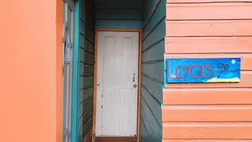 Une étroite entrée en bois avec une porte blanche, une enseigne bleue sur laquelle est écrit le mot « LOVAS », et un paillasson rouge au bas de l’entrée.