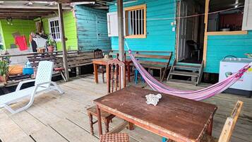 Una terraza de madera con una mesa, sillas, una hamaca y una pequeña mesa con mantel de encaje.