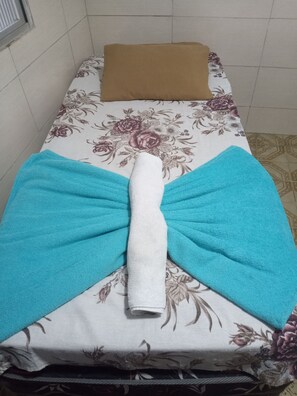 Una cama con colcha floral, almohada marrón y toalla blanca doblada.