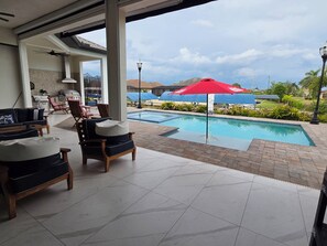 Un espace aménagé au bord de la piscine, avec des chaises longues, un coin repas et une vue sur un quartier résidentiel.