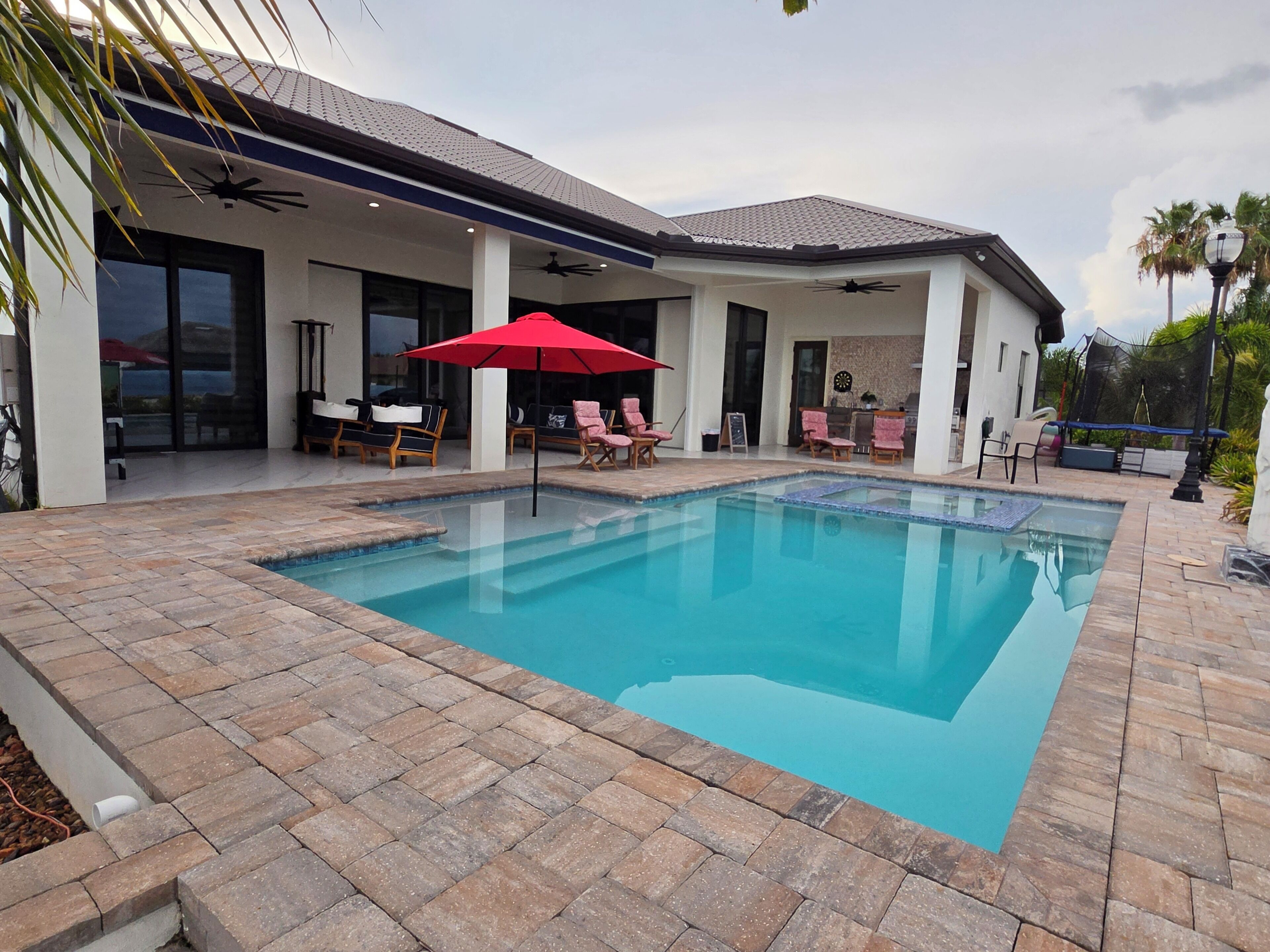 A swimming pool with a tiled deck, outdoor seating, and a covered patio area.