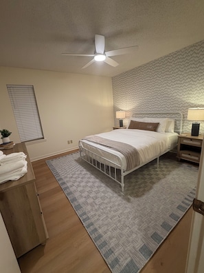A bedroom with a bed, a ceiling fan, a bedside table with a lamp, a nightstand, a window with blinds, and a wooden dresser. - Relax with a Ranch Water and enjoy the gorgeous Texas sunset after a long day (Vernon)