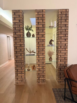 A room with a brick column structure, wooden flooring, a glass shelf with decorative items, and a brown leather chair. - Relax with a Ranch Water and enjoy the gorgeous Texas sunset after a long day (Vernon)
