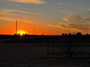 A sunset over a rural landscape with power lines and a fence.