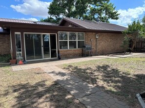 A brick building with a metal roof, a covered patio, and a paved walkway.
