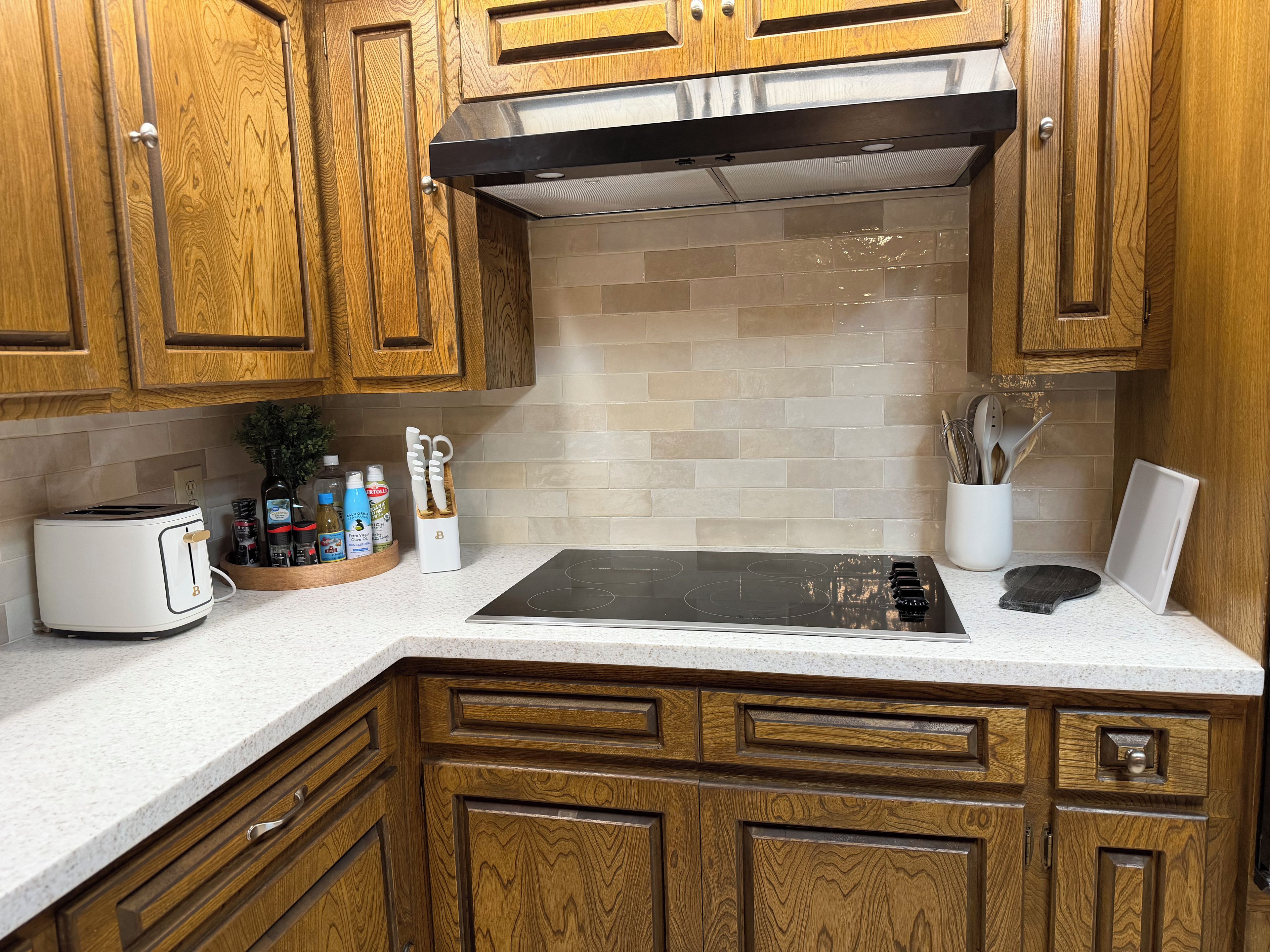 A kitchen with wooden cabinets, a stainless steel range hood, a white induction cooktop, and a countertop with a toaster and a knife block.