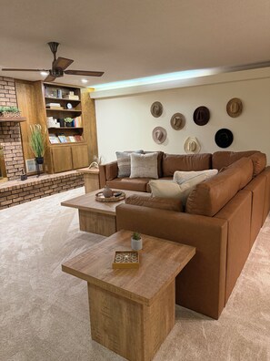 A cozy living room with a brown leather sofa, a wooden coffee table, and a brick fireplace. - Relax with a Ranch Water and enjoy the gorgeous Texas sunset after a long day (Vernon)