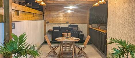 Une terrasse extérieure avec une table et des chaises en bois, un barbecue et des plantes en pot.