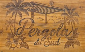 A wooden sign with carved palm trees and a beach scene, featuring the text 'Pergola du Sud'. - Accommodation, 12 min. from the lagoon, spa, air-conditioned, sleeps 4, 3 terraces, parking (Saint-Pierre)