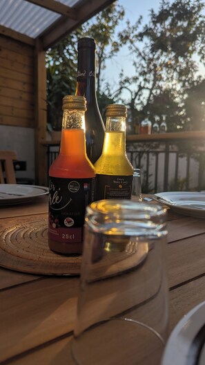 Two bottles of wine on a wooden table with a glass of water in the foreground. - Pergola du Sud - Accommodation - 12 minutes from the lagoon, air-conditioned, sleeps 4, 2 terraces (Saint-Pierre)