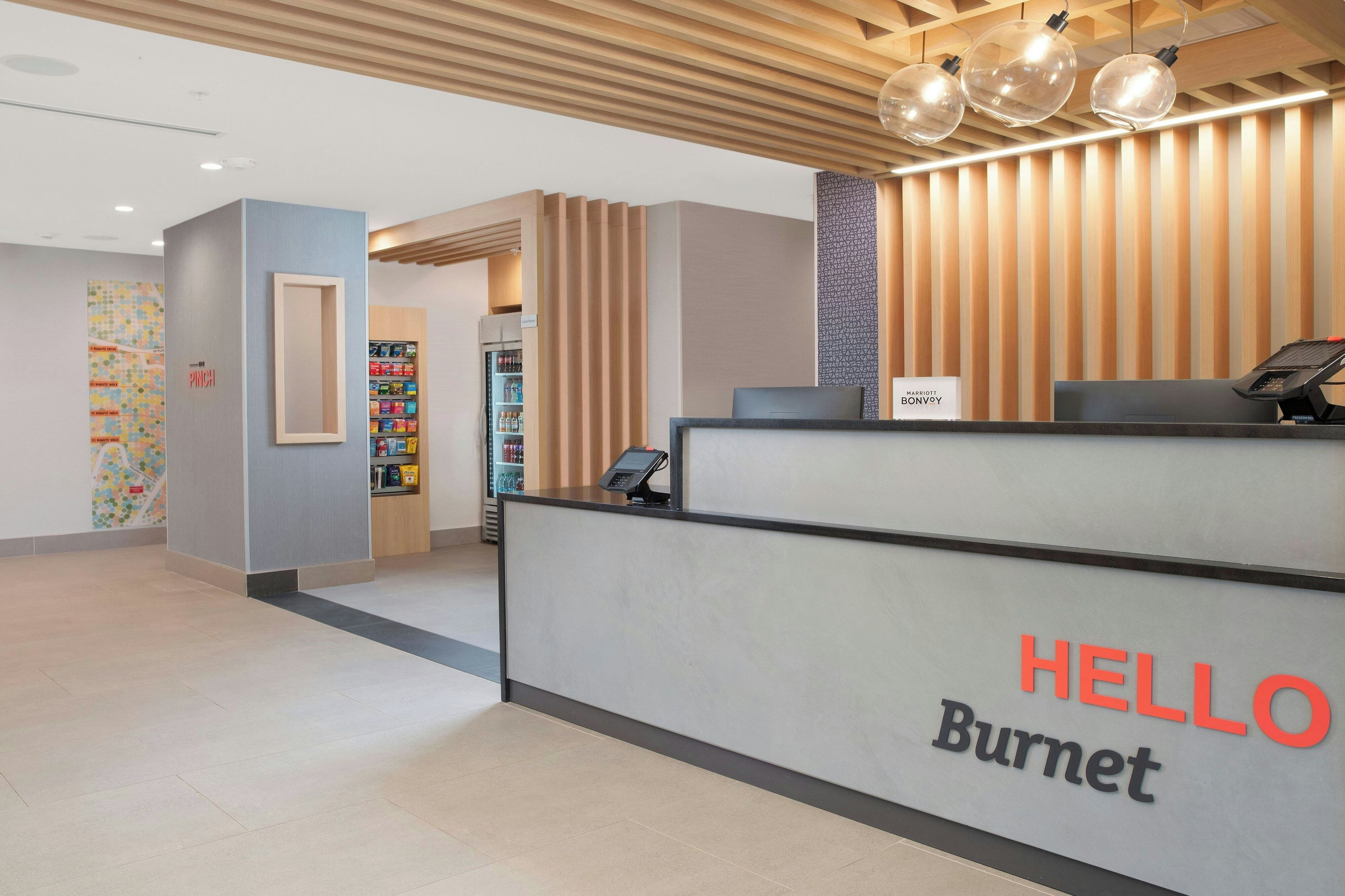 Un comptoir d’accueil avec une enseigne indiquant « BONJOUR Burnet », un distributeur automatique et un mur orné d’un motif géométrique.