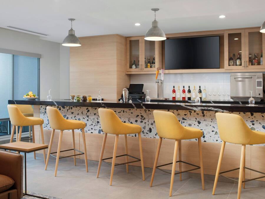 Una cocina moderna con barra, taburetes, televisor de pantalla plana y espacio para botellas de vino.
