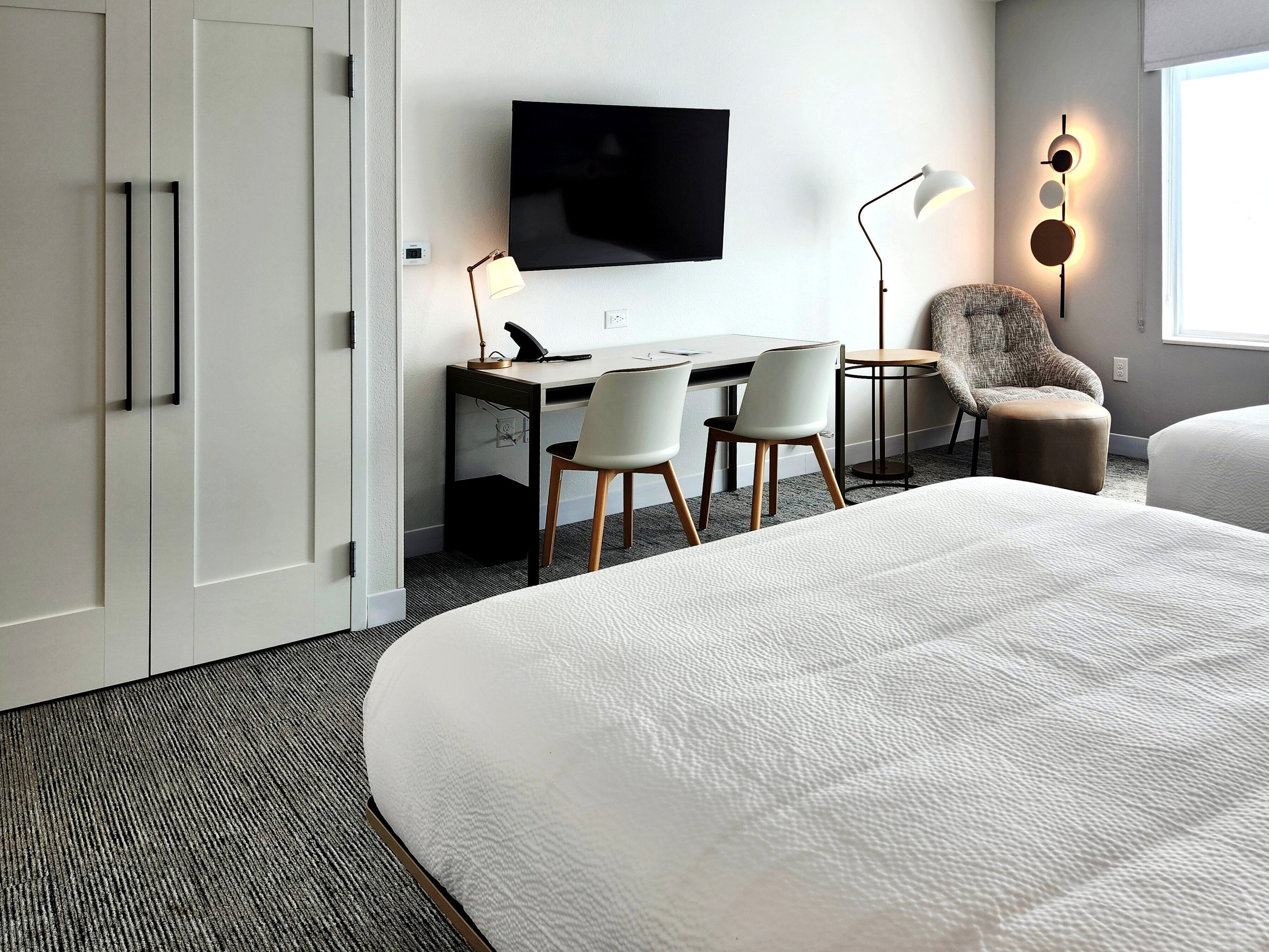 A hotel room with a bed, a desk with two chairs, a television, and a lamp.