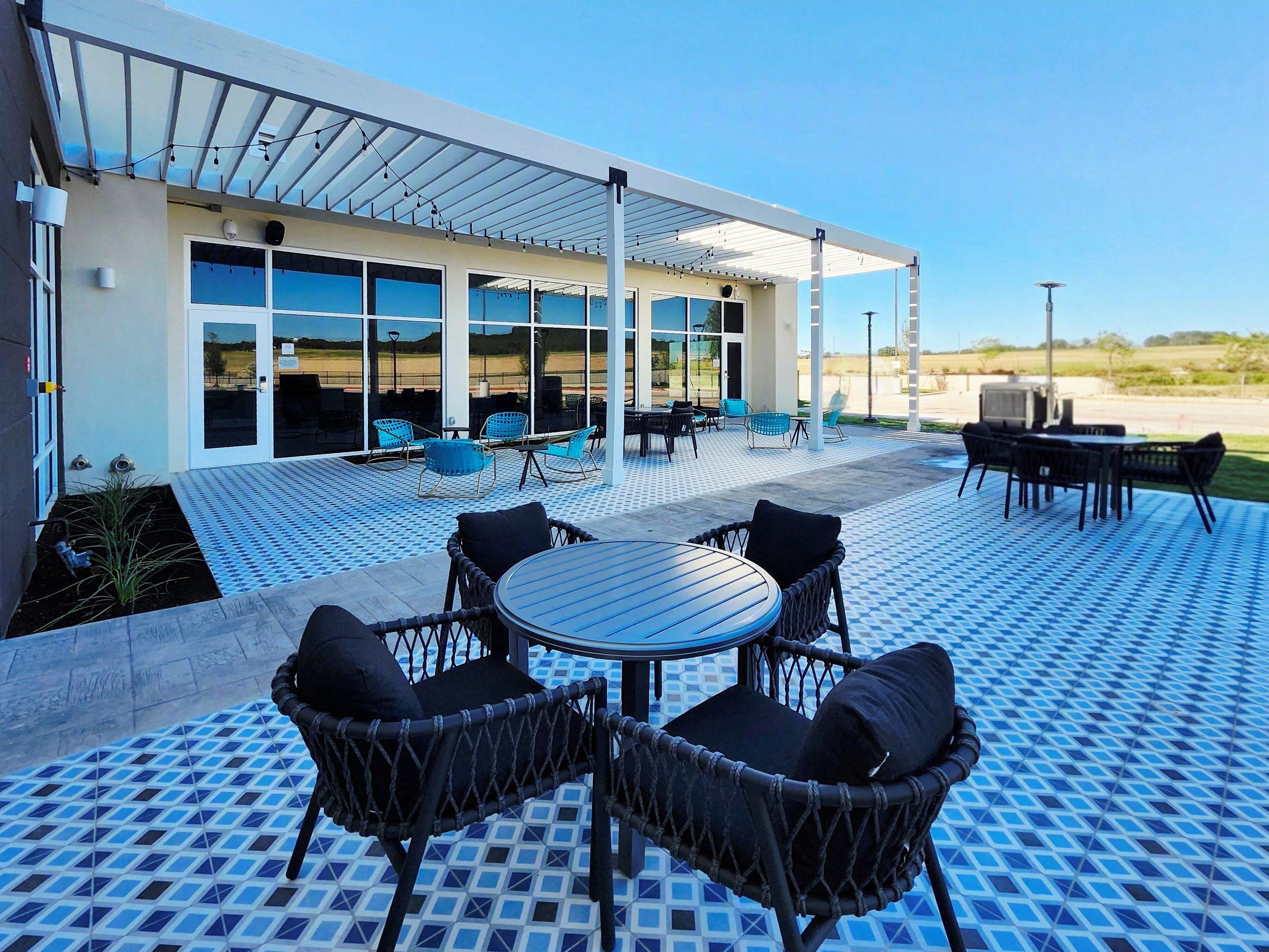 An outdoor patio with a covered seating area, a pool, and a building with large windows.