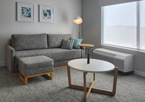 Un salon moderne avec un canapé gris, une table ronde en bois et un lampadaire.