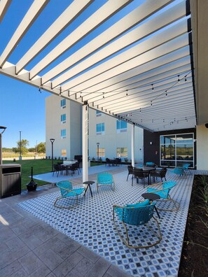 Un espace extérieur aménagé en terrasse, avec des sièges, un barbecue et une partie couverte dotée d’un sol à motifs.