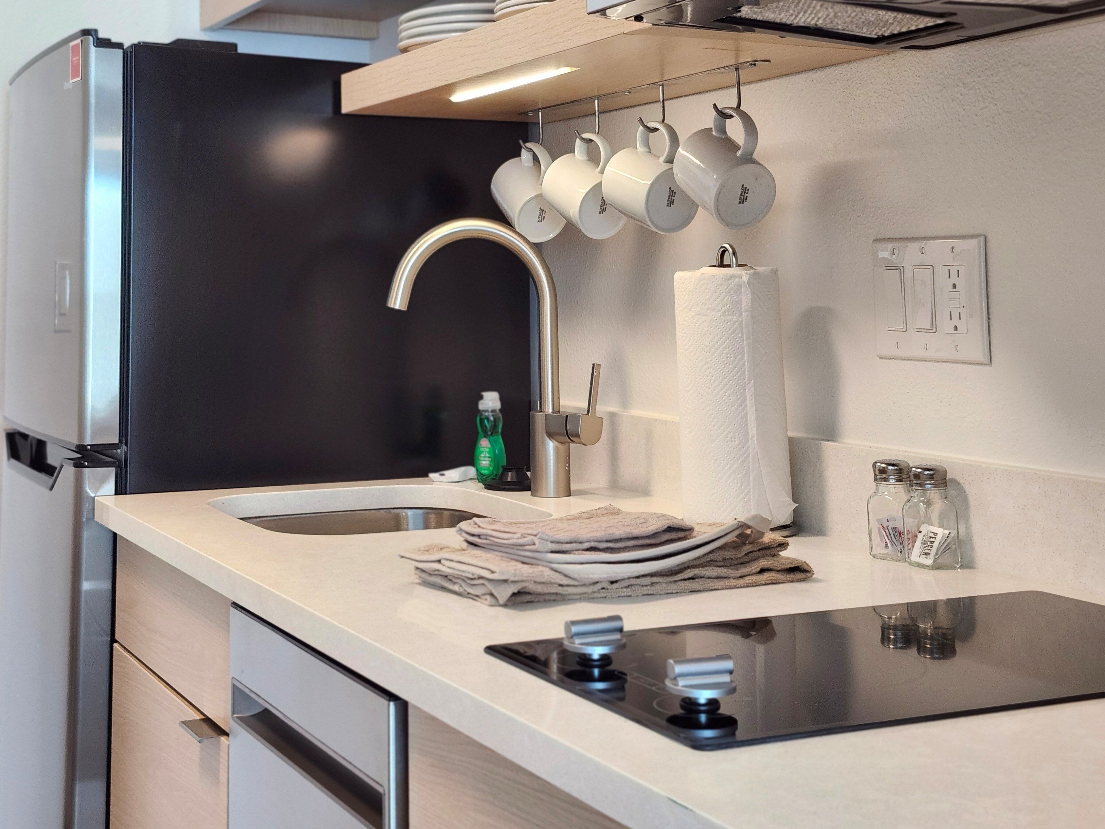 A modern kitchen with a stainless steel refrigerator, a sink with a faucet, a stack of towels, and a tea kettle hanging above the counter.