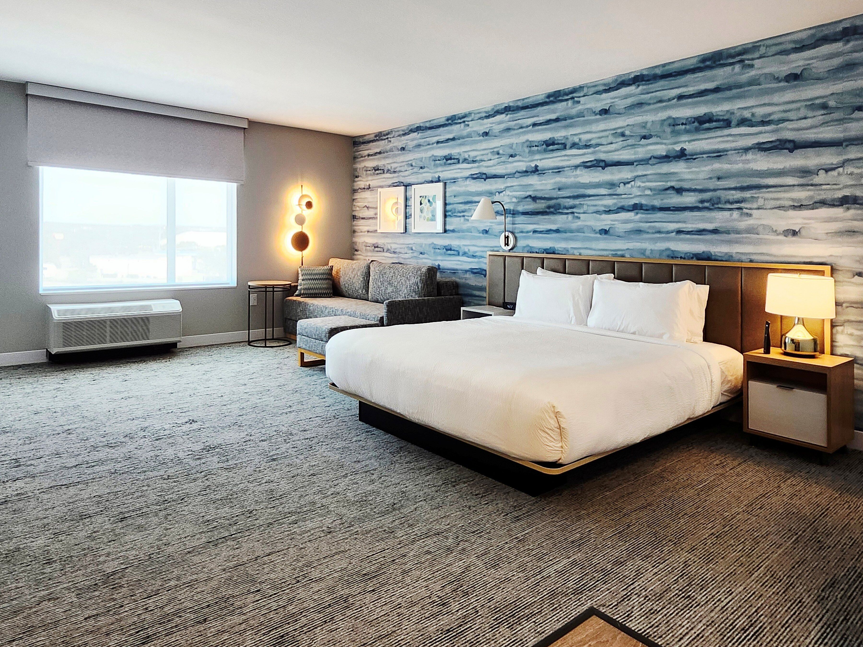 A hotel room with a large bed, a sofa, a small table, and a wall with a blue abstract design.