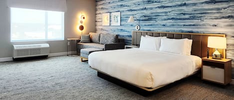 Habitación de hotel con una cama grande, un sofá, una mesita y una pared con un diseño abstracto azul.
