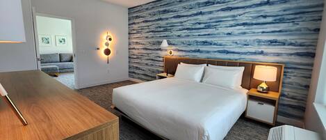 A hotel room with a bed, bedside tables, a desk, and a wall with a blue abstract design.