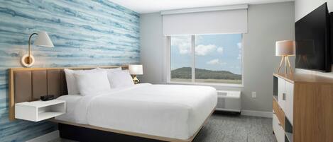 Ein Hotelzimmer mit einem großen Bett, einem Fernseher, einem Fenster mit Blick und einer Wand mit blauem abstrakten Design.